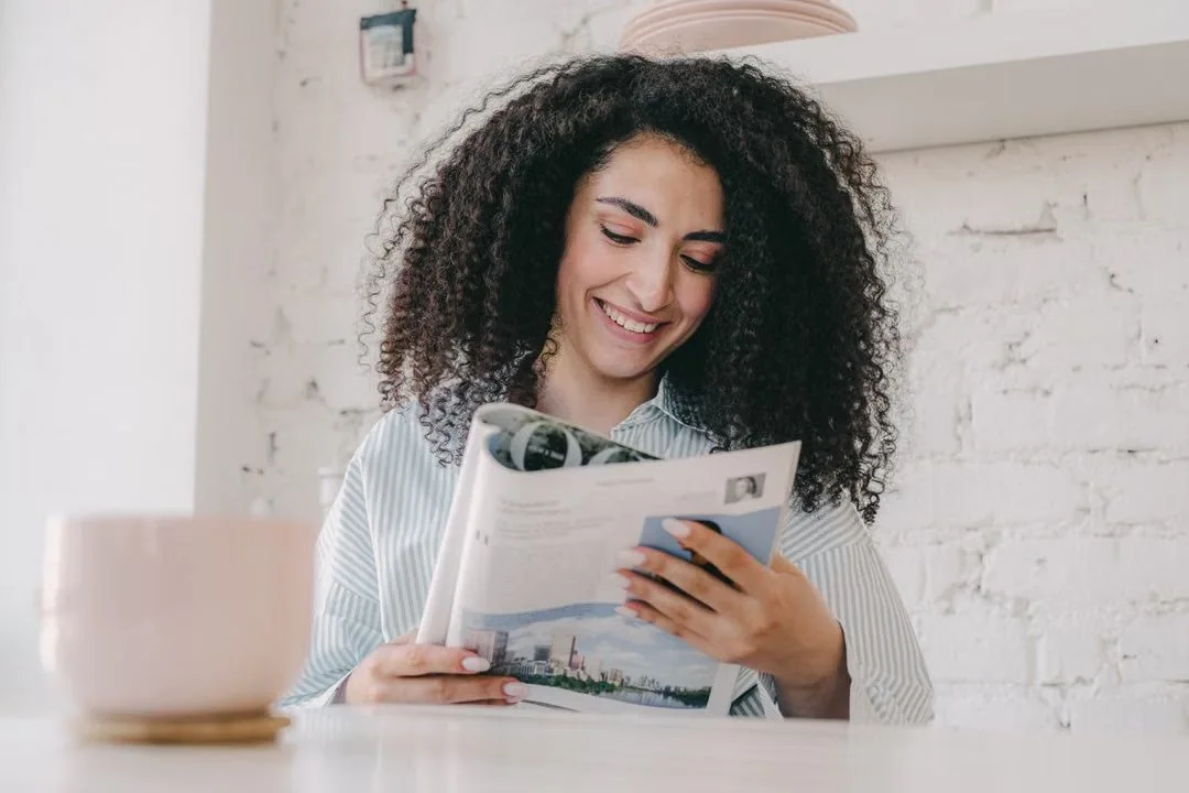 Woman reading a newspaper at a table.