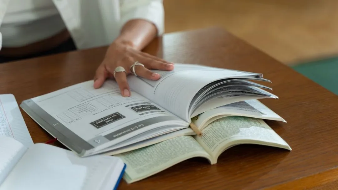 Hand turning the pages of an open reference book on a desk.