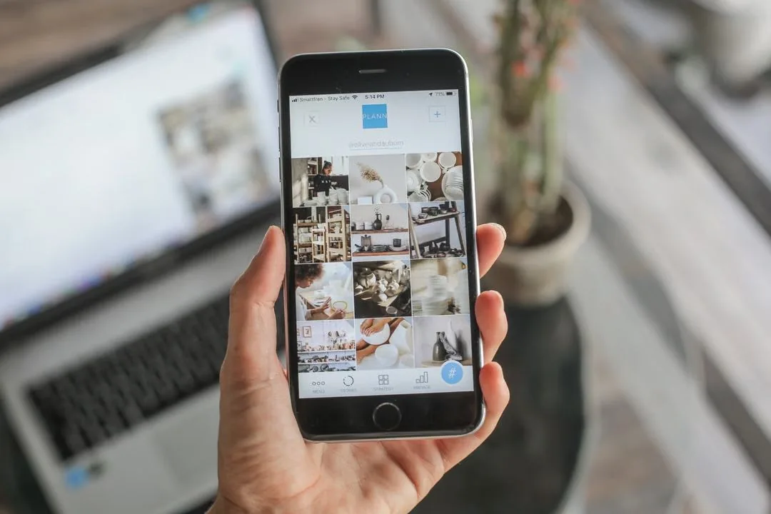 Hand holding a smartphone showing a grid of social media posts.