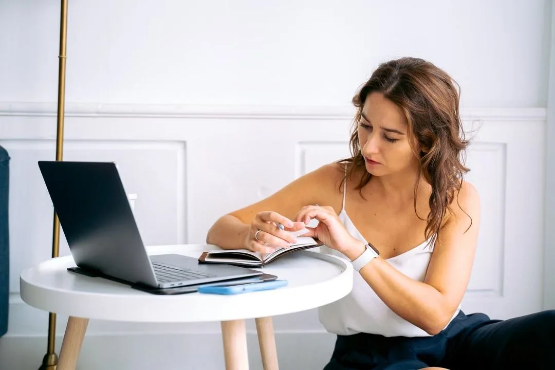 Woman checking her phone beside an open laptop.