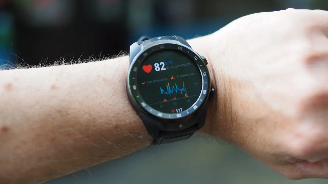 Smartwatch displaying heart-rate and fitness data on a wrist outdoors.