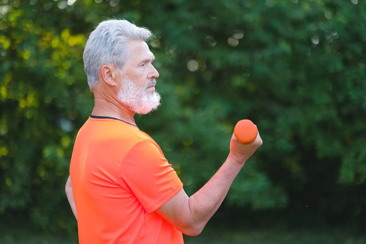 Older man strength training outdoors with a dumbbell.