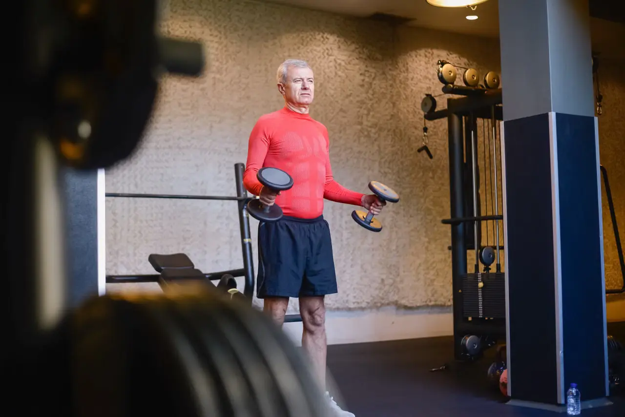 Older man lifting dumbbells in a gym.