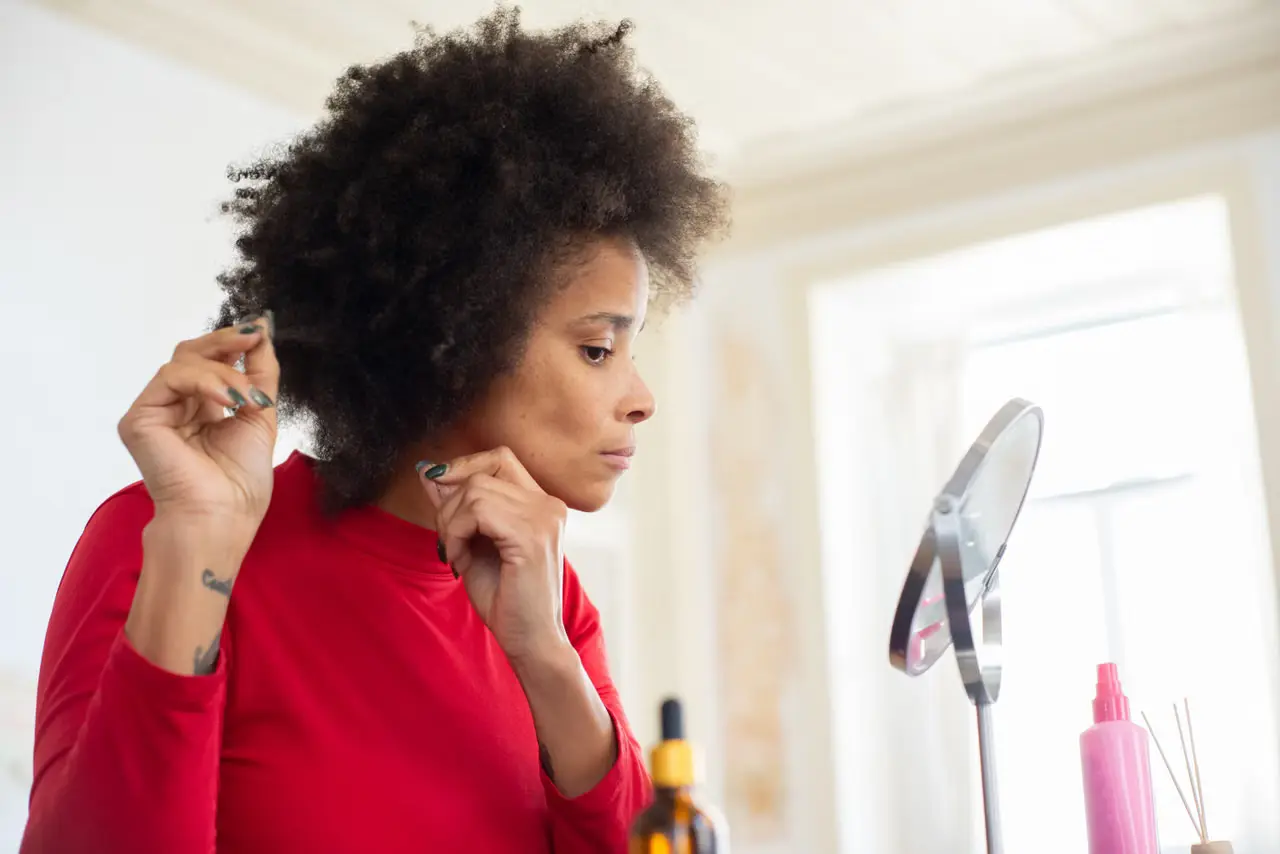 Adult checking and styling natural hair in a mirror during a personal care routine.