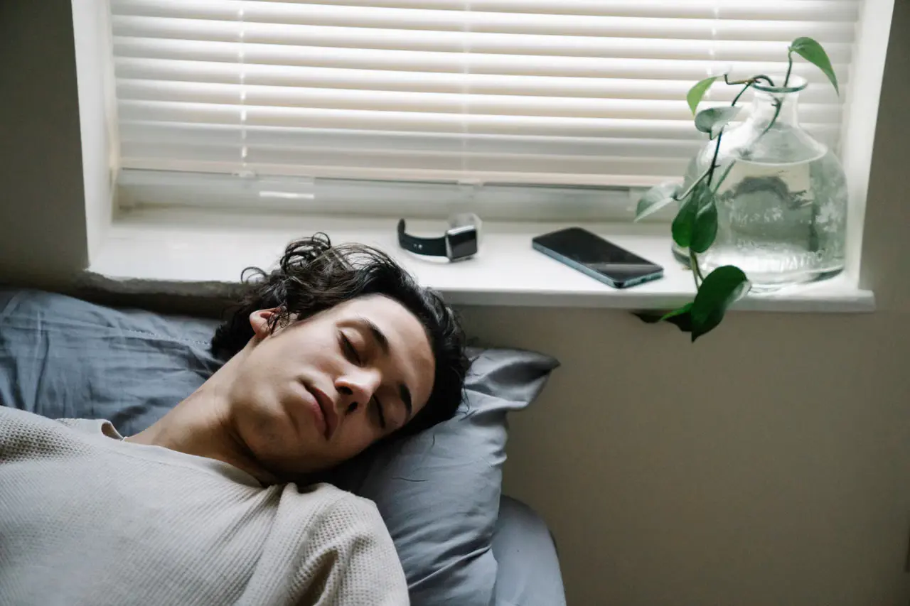 Person sleeping in bed with a smartwatch nearby for overnight sleep tracking.